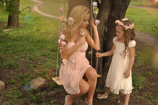 A beautiful blond mother with a small daughter girl snuggling on nature background of green and purple flowers and colorful soap bubbles May, the head wreaths of wild flowers