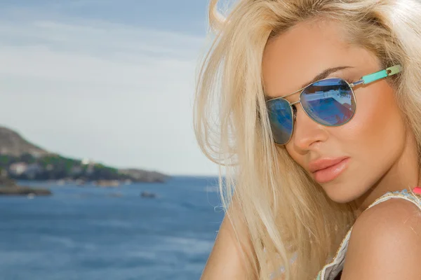 Beautiful blond hair sexy woman young girl model in sunglasses and elegant color  with crystals sweatshirt, top around the pool with a balustrade overlooking the sea and the island of Santorini