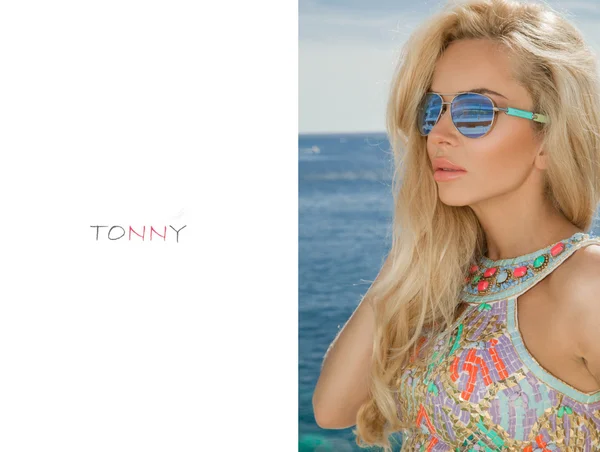 Beautiful blond hair sexy woman young girl model in sunglasses and elegant color  with crystals sweatshirt, top around the pool with a balustrade overlooking the sea and the island of Santorini