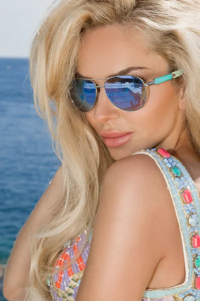 Beautiful blond hair sexy woman young girl model in sunglasses and elegant color  with crystals sweatshirt, top around the pool with a balustrade overlooking the sea and the island of Santorini