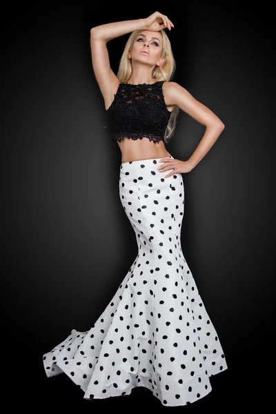 Beautiful blond with long curly hair young woman in the white model black ball gown, a polka color with a long train on a black background