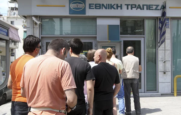 People stand in a queue to use the ATMs of a bank