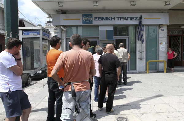 People stand in a queue to use the ATMs of a bank