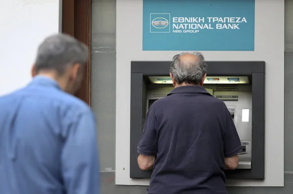 People stand in a queue to use the ATMs of a bank