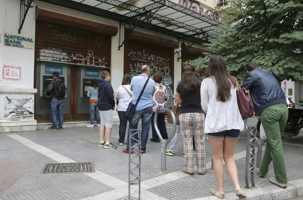 People stand in a queue to use the ATMs of a bank