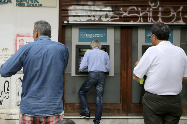 People stand in a queue to use the ATMs of a bank