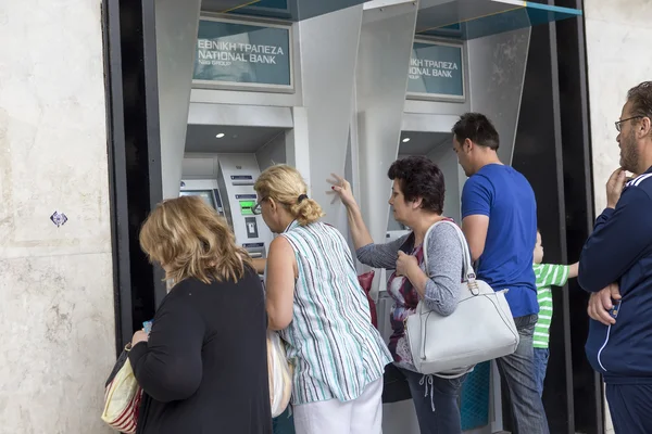 People stand in a queue to use the ATMs of a bank. Greece\'s frau