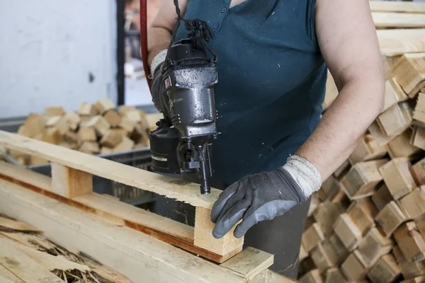 Craftsman puts nails in a piece of wood at a woodworking factory