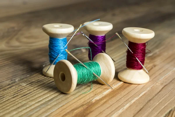 Spools of thread with needles on wooden background. Old sewing a