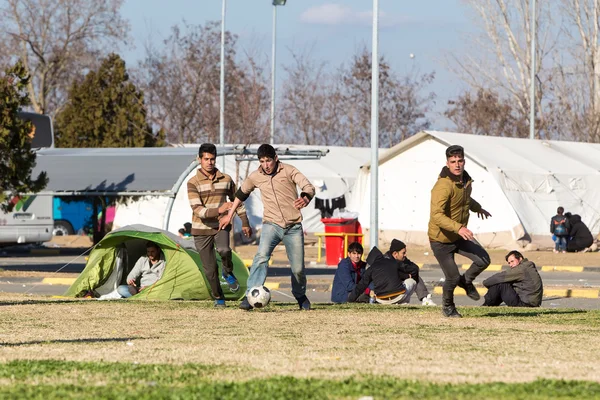 Migrants and refugees play football in the parking lot of a gas