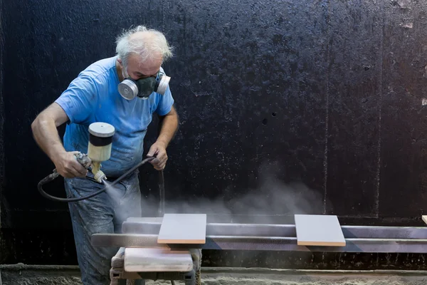 Man worker painting wooden board with spray gun wearing protecti
