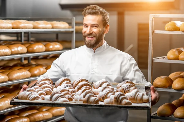 Handsome baker holding tray full of freshly baked croisants
