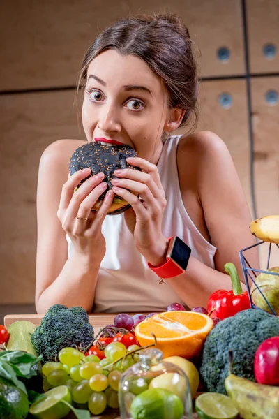 Woman eating burger at the table full of healthy food