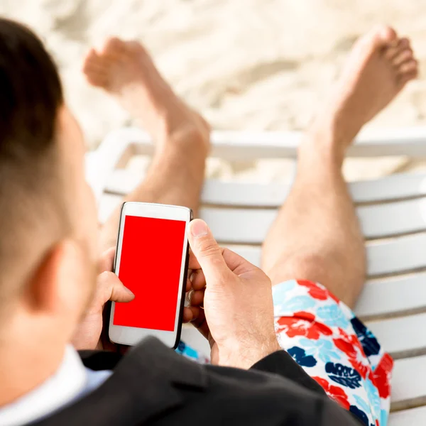 Businessman holding cellphone on the beach