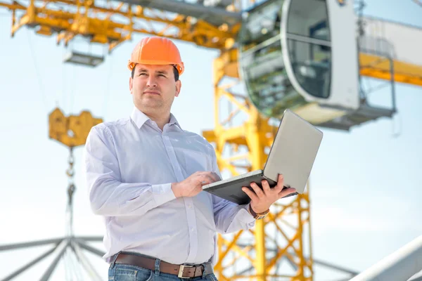 A foreman with laptop at the construction supervising the project.