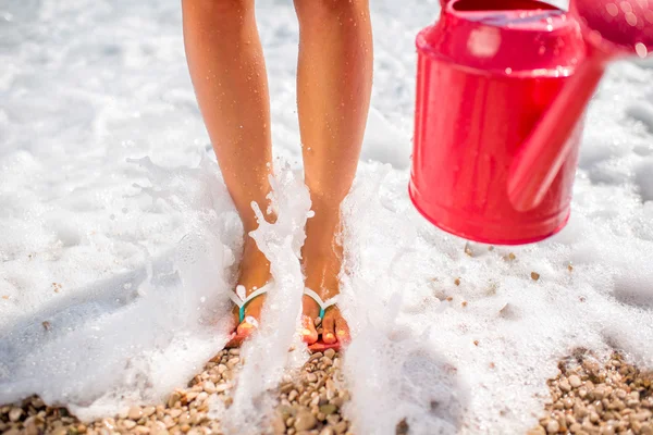 Womans legs with watering can on the beach