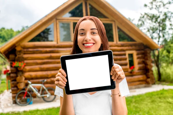 Woman showing digital tablet near the wooden cottage.