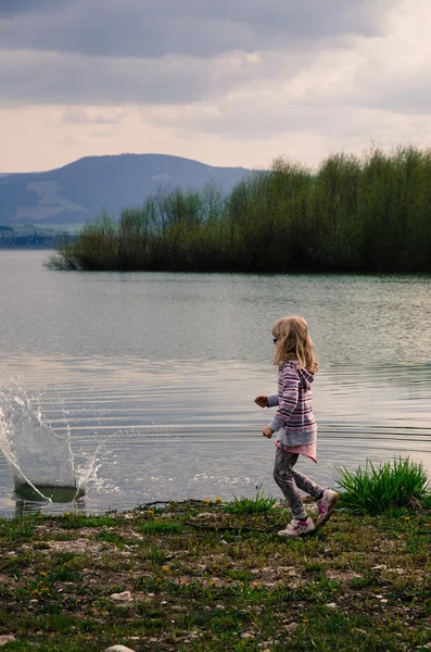 Girl throwing stones into pond