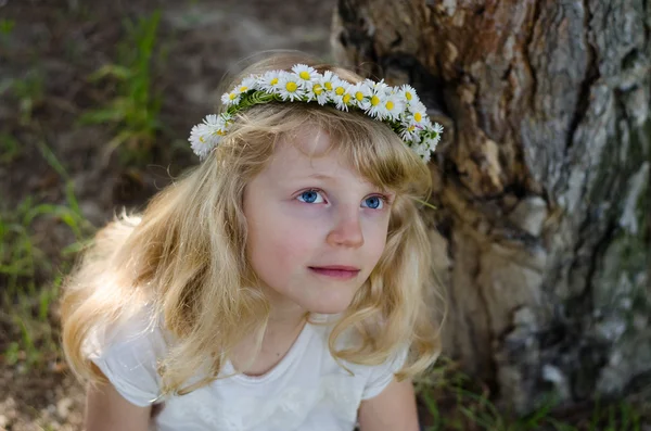 Smiling blond girl with big blue eyes and with daisies on head