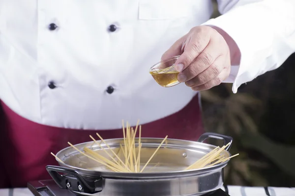 Chef pouring olive oil to spaghetti boiled in the pan