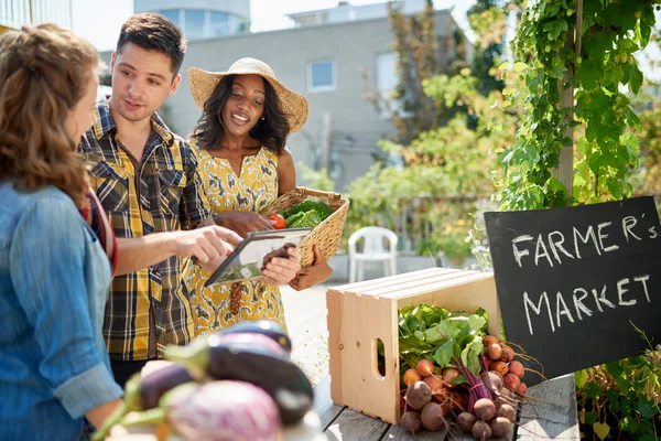 Friendly woman tending an organic vegetable stall at a farmers market and selling fresh vegetables from the rooftop garden