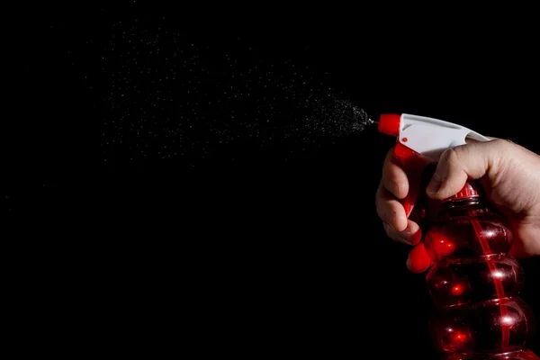 A human hand with a spray gun sprays water on a dark background