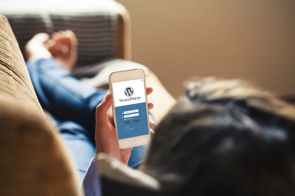 Woman using Wordpress app in a mobile phone while lying in a sofa.