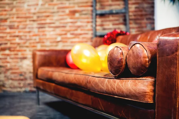 Close up of leather sofa with party balloons. Brick wall background.