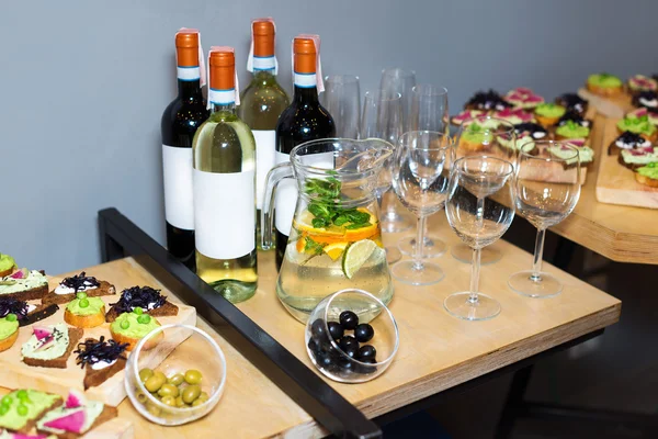 Wooden tray of appetizers at a banquet on a decorated tea table with red and white wine and carafe of fruity beverage with mint and lemon. Beautifully decorated table set  in the restaurant.