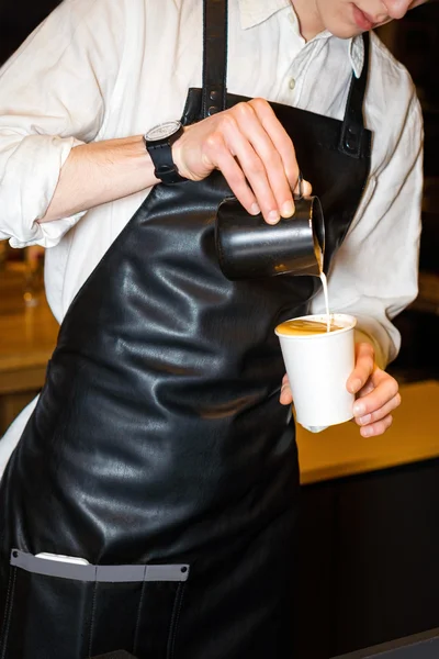 Barista making coffee. Hand of barista making latte or cappuccino coffee pouring milk in paper cup and making latte art.