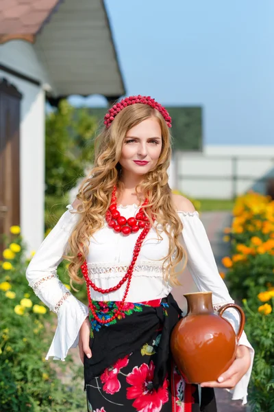 Woman in national ukrainian traditional costume holding a clay jug and welcoming guests