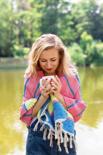 Woman wrapped in a blanket drinking tea in the forest