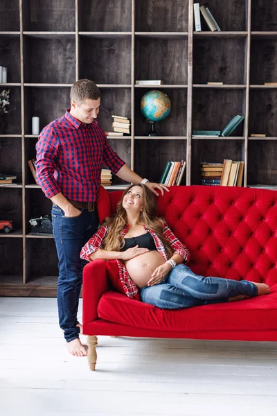 Beautiful pregnant couple relaxing on sofa at home together. Happy family, man and woman expecting a child.