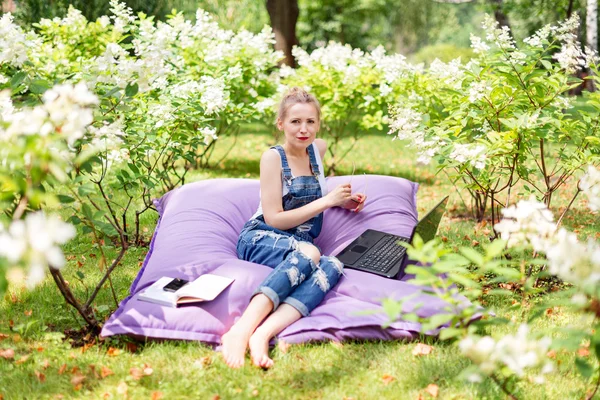 Freelancer working in the garden. Writing, surfing in the internet. Young woman relaxing and having fun in park area. Distance education, freelance concept.