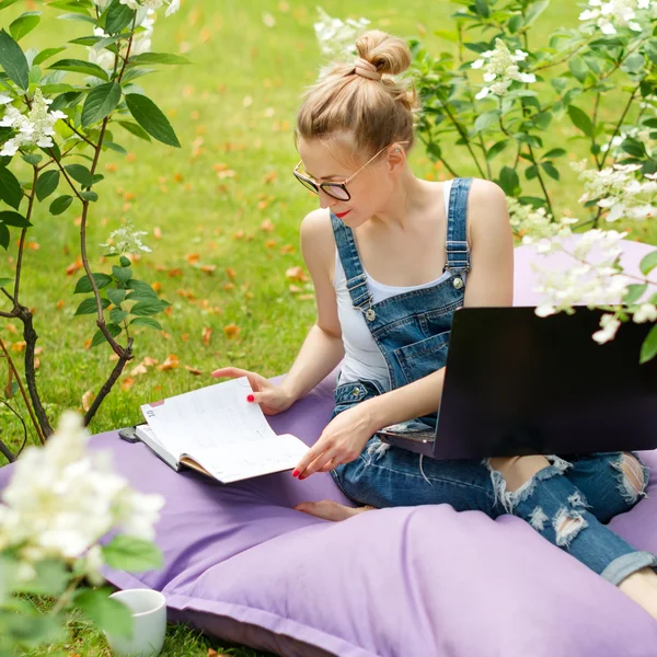 Freelancer working in the garden. Writing, surfing in the internet. Young woman relaxing and having fun in park area drinking coffee. Distance education, freelance concept.