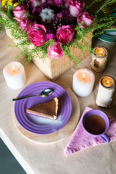 Piece of delicious chocolate mousse cake on colorful plate on wooden table background. Table setting with flowers and candles for tea party. Selective focus.