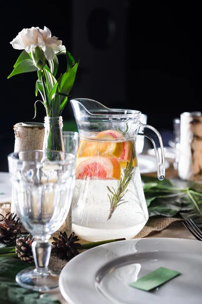 A carafe of fruity beverage with rosemary and lemon on a decorated table ready for dinner. Beautifully decorated table set for wedding or another event in the restaurant.