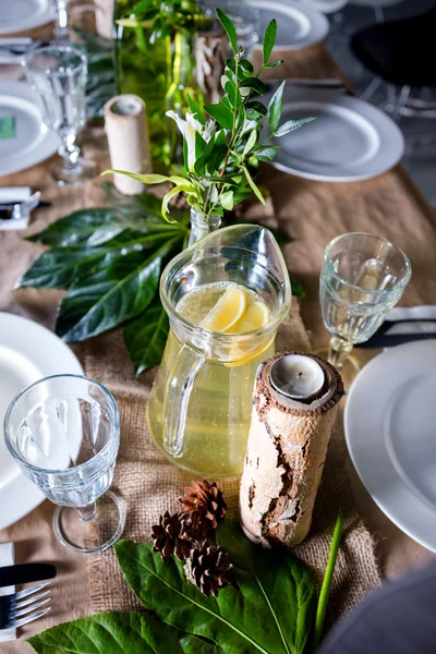 A carafe of fruity beverage with rosemary and lemon on a decorated table ready for dinner. Beautifully decorated table set for wedding or another event in the restaurant.