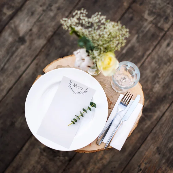 Paper menu on decorated table ready for dinner. Beautifully decorated table set with flowers, plates and serviettes for outdoor wedding ceremony or another event in the restaurant.