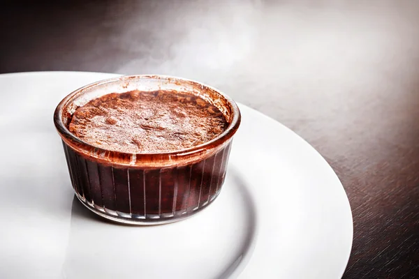 Freshly baked steaming hot dessert chocolate fondant lava cake served on white plate. Famous French dessert on dark wooden table top view.