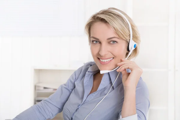 Attractive smiling middle aged woman in blue calling with headse