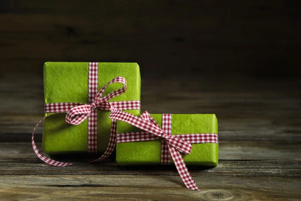 Two green gifts with red white checkered ribbon on wooden backgr