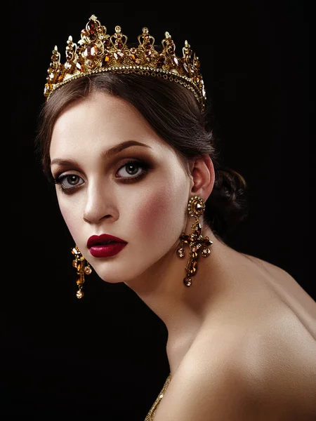 Beautiful brunette girl with a golden crown, earrings and profes