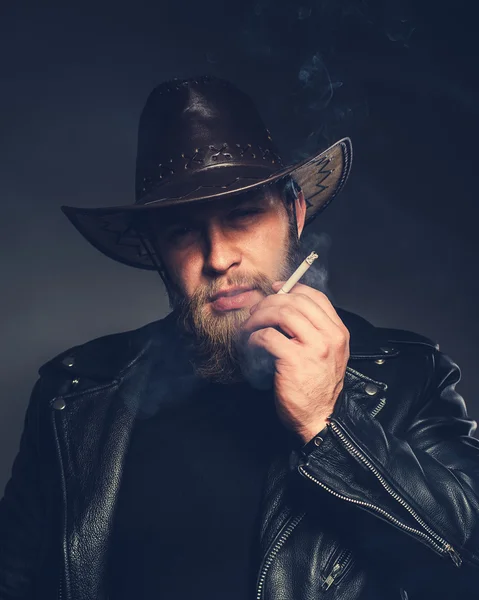 Smoking man with a beard and mustache wearing a cowboy hat.