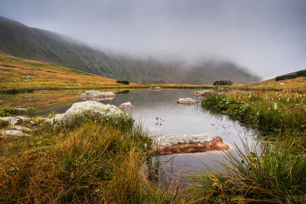 Small Tarn with Rocks in Foggy Mountains