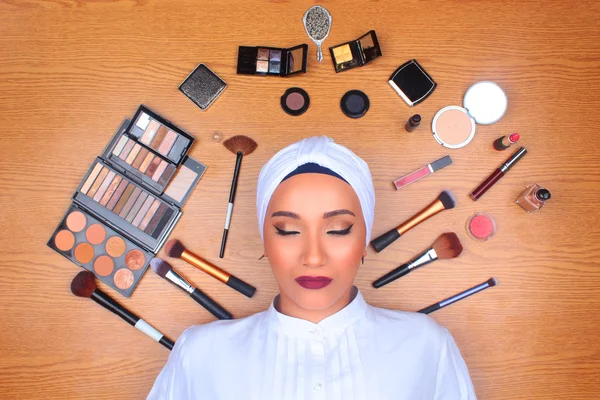 Woman in full makeup surrounded by makeup