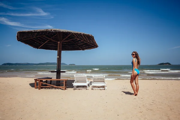 Woman resting on a tropical beach near deck chair and sun umbrel