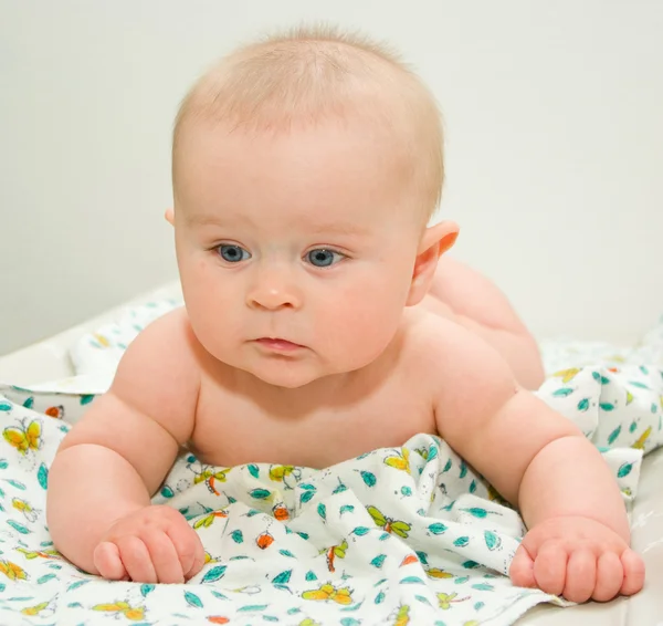 Thoughtful infant with big grey-blue eyes laying on a blanket on a grey background