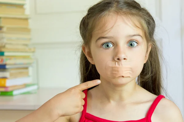 The frightened little girl shows a finger on his mouth glued with adhesive tape