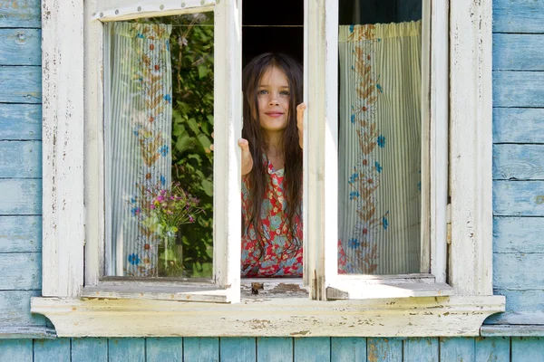 Happy little girl opens a window of rustic house in the early sunny morning